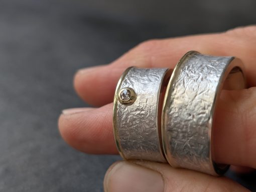 Trauringe aus Silber 925 mit massivem Goldrand und rose-cut Diamant 2 Eheringe mit Goldrand und Diamant werden zwischen zwei Fingern gehalten