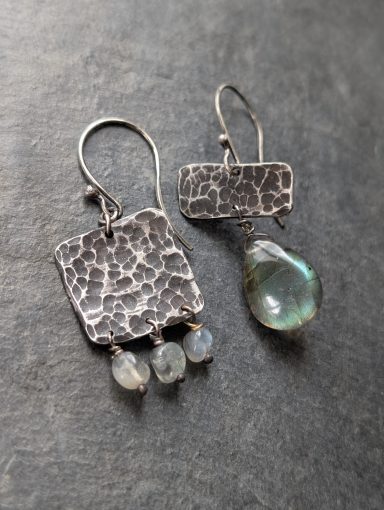 Asymmetrische Ohrringe mit roher dunkler Textur und Labradorit 2 unterschiedliche asymmetrische Ohrringe mit geschmiedeter oxidierter Textur und Labradorit liegen nebeneinander